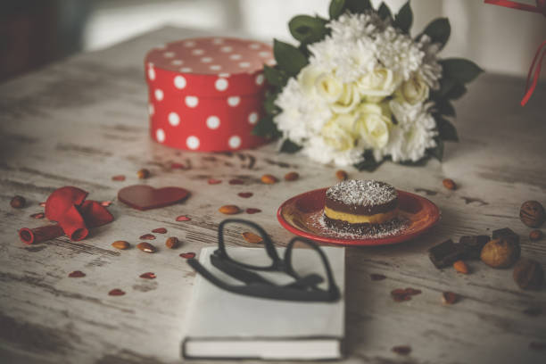 High angle view of romantic decorations with vegan cake, white flowers, gift box and dry fruits for Valentine's evening.