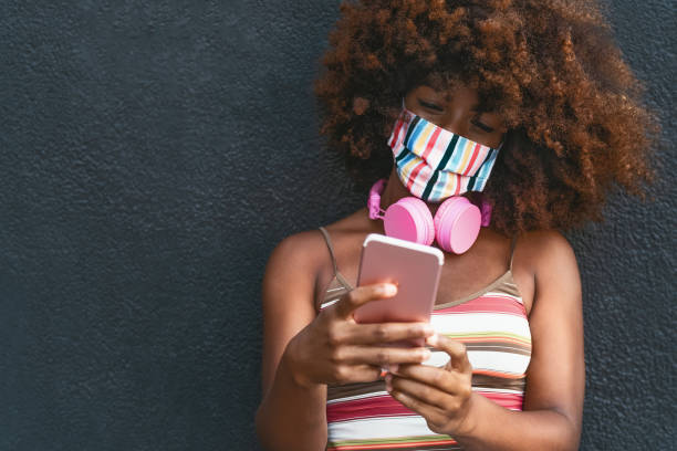 istock Happy Afro woman using mobile smartphone while wearing face colored mask outdoor 1280768714