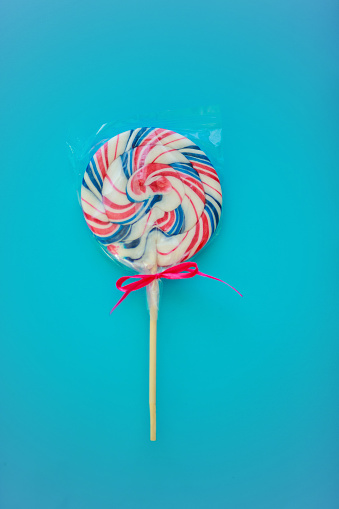 Copyspace of circular lollipop in its transparent package and placed against a light blue background for boys.