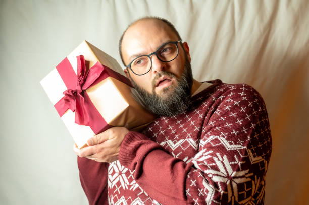 istock man carefully holds a present to his ear to find out what is inside 1280772449
