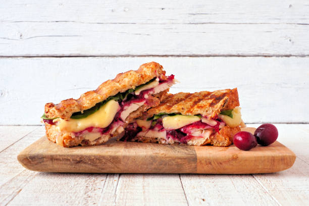 peru grelhado, cranberry e sanduíche de brie em uma tábua de servir contra madeira branca - sandwich turkey cranberry cheese - fotografias e filmes do acervo