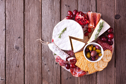 Platter of assorted meats, cheeses and appetizers. Overhead view on a rustic wood background.