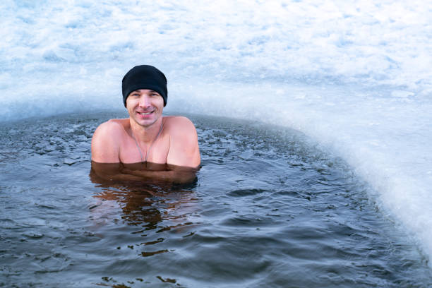 winterschwimmen. der eiskalte lächelnde mann im hut steht im winter im kalten wasser. kopieren spase - ein bad nehmen stock-fotos und bilder