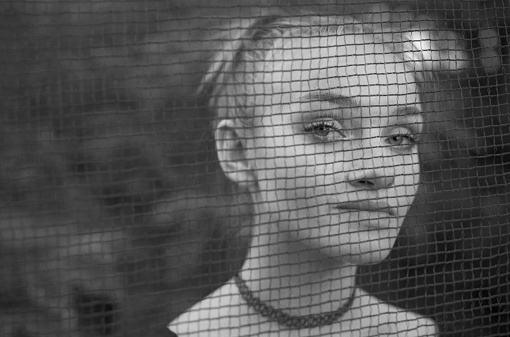 Close-up of a young woman face through a protective mesh in the forest in Kyiv, Kyiv City, Ukraine