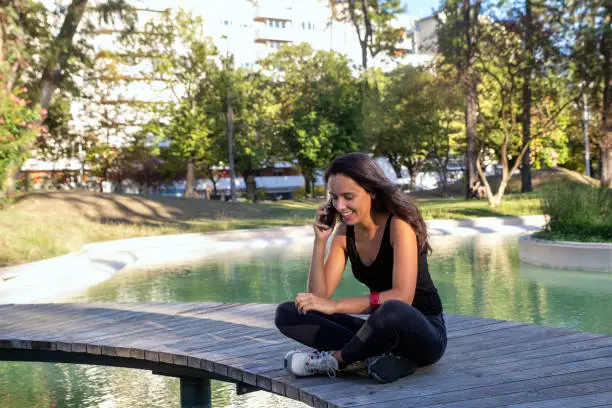 Young adult brunette female with long black hair happily talking on the phone sitting in the park