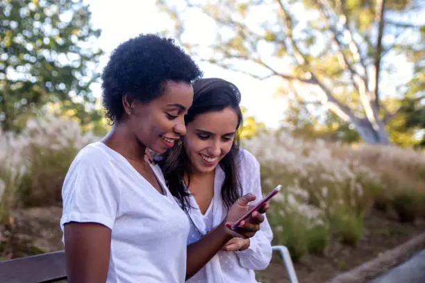 Two female friends sitting on a bench interacting with a mobile phone