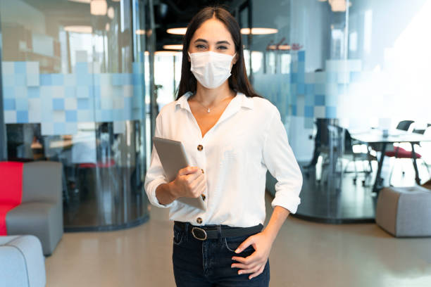 woman is working with mask because of pandemic - business looking at camera office new imagens e fotografias de stock