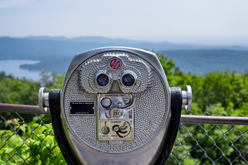 A quarter operated binoculars on top of Prospect mountain overlooking lake george, new york on a sunny day.