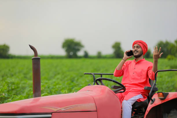 istock young indian farmer sitting on tractor and talking on smartphone at field 1280782232