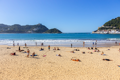 San Sebastian, Spain - 10/10/2019: Unknown people relax on the beach called La Concha. Beautiful bay of Biscay in San Sebastian. Wide aerial beach on sunny day. Healthy and relax lifestyle. Scenic seascape in morning. Nature of Basque country.
