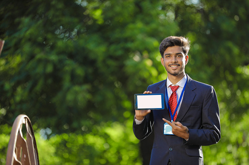 Young indian banker showing smartphone at field