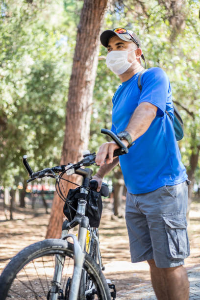 istock Man wearing protective face mask standing next to bike at park 1280793083