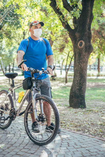 istock Man wearing protective face mask standing next to bike at park 1280793123