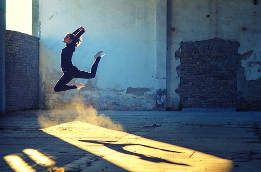 Ballerina jumping and dancing in abandoned building on a sunny day.