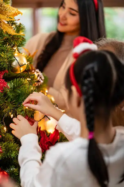 Close up hand little girl decorating a Christmas tree with mom in background preparing for season greeting of Merry Christmas and Happy Holidays. Multigenerational Family engage and happiness concept.