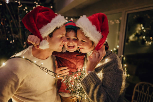 The strongest bond Photo of a family with one child wrapped in Christmas lights,  celebrating holidays on the balcony of their apartment; throwing an unforgettable Christmas party at home. family christmas party stock pictures, royalty-free photos & images