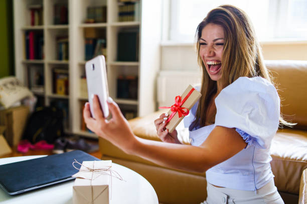 istock One Happy millennial caucasian woman sitting alone at home making video call smiling while showing gift wrapped present - Selective focus on hand 1280805334