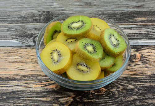 Raw fresh golden yellow and green kiwi fruit slices in glass bowl on table