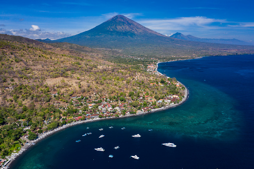 Landscape taken by drone of the peaceful and sleepy fishing village of Amed in Karangasem province of Bali in Indonesia with the Agung volcano standing on the horizon.