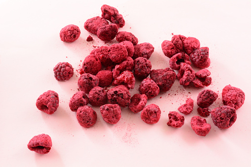 Pile of freeze dried red raspberries fruit on pink background
