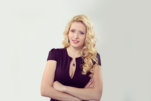 Skeptical. Closeup portrait confused skeptical shy timid woman looking at you camera.  Caucasian Business person in black formal dress, long blond curly hair isolated light grey gray studio background