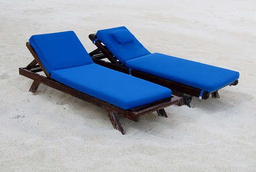 Two empty sun loungers on a white sandy beach.