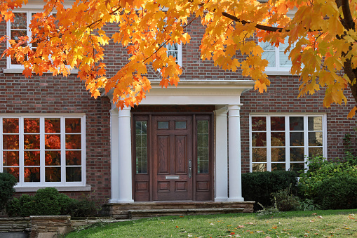 front door of traditional two story brick house with maple tree in brilliant fall color