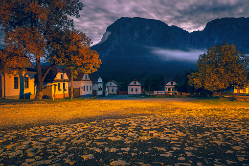 Beautiful rural street with traditional houses in row at dawn. Torocko village and stunning Piatra Secuiului mountain in background at sunrise, Rimetea, Alba county, Transylvania, Romania, Europe