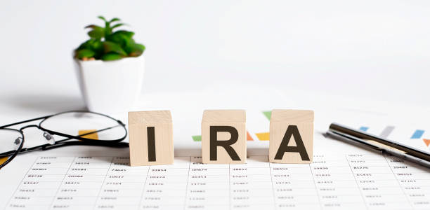 IRA word concept written on the wooden blocks, cubes on a light table with flower ,pen and glasses on chart background stock photo
