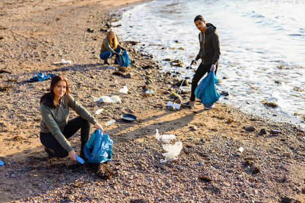 istock Young woman in a team picking up plastic garbage in bag at beach 1280857687