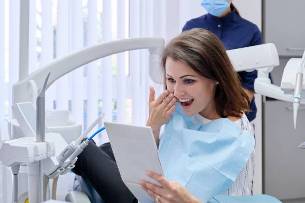 Happy middle aged woman with doctor dentist looking in mirror at teeth stock photo