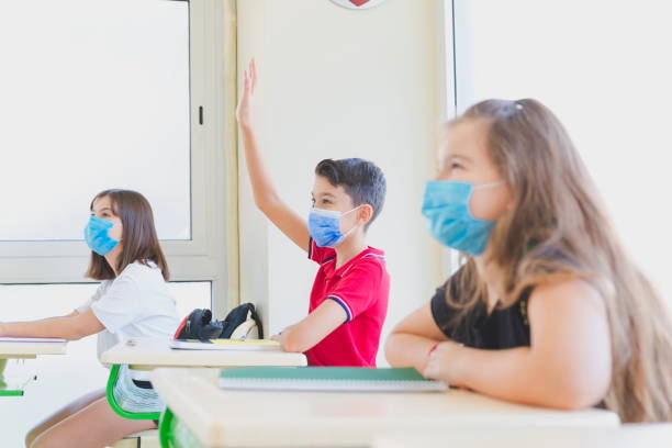 istock Elementary students raising hands during a lesson and wearing face masks 1280865216