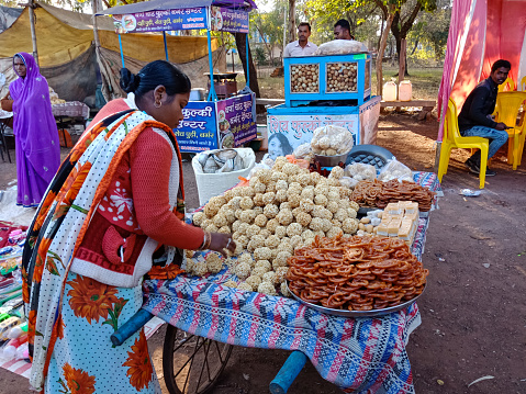 DISTRICT KATNI, INDIA - FEBRUARY 02, 2020: an indian man selling traditional Jalebi sweet to the customer at carriage shop during village bazaar festival Fest event.