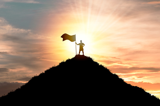 Business achievement objective  target and successful  concept , Silhouette Man standing and holding flag on top of mountain with cloud sky and sunlight.