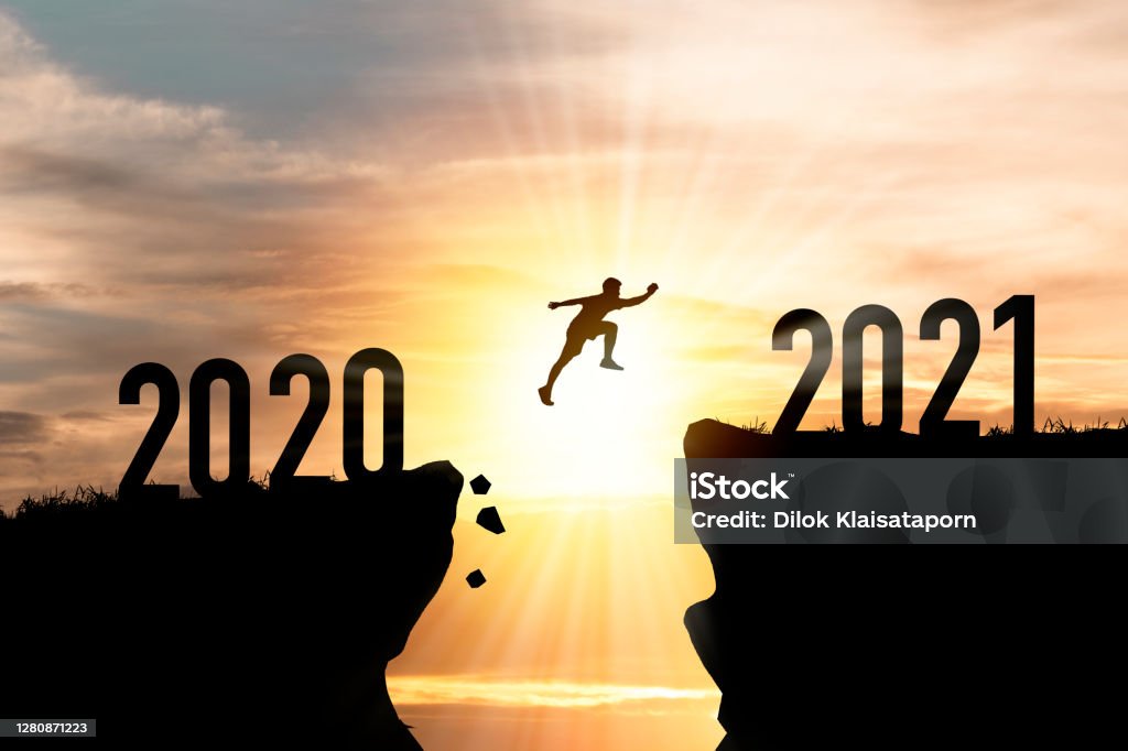 Welcome merry Christmas and happy new year in 2021,Silhouette Man jumping from 2020 cliff to 2021 cliff with cloud sky and sunlight. 2021 Stock Photo