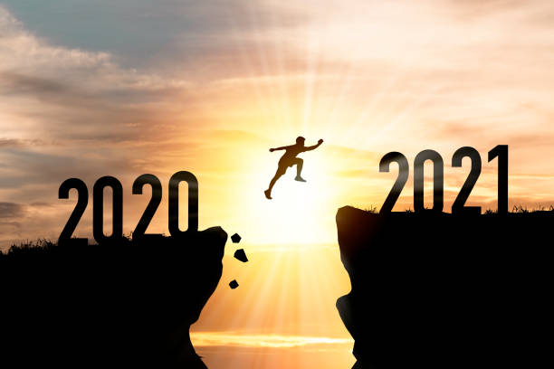 歡迎聖誕快樂和新年快樂在2021年,剪影人跳躍從2020懸崖到2021懸崖與雲的天空和陽光。 - 2021 圖片 個照片及圖片檔
