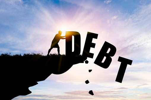 Eliminate or get rid of debt concept , Silhouette man pushed off debt wording a cliff with blue cloud sky and sunlight.
