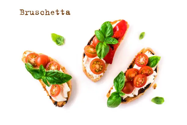 Bruschetta sandwiches with tomatoes, cream cheese, grilled paprika and basil isolated on white background, top view, copy space. Traditional italian snack - grilled bruschetta toasts.