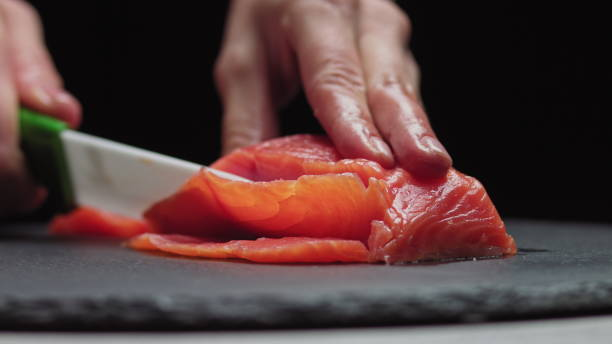 sushi chef rebana salmón fresco en el bar de sushi. chef cortando filete de salmón en cocina profesional. manos de chef de primer plano cortando la rebanada de pescado fresco en cámara lenta. hombre profesional cortando peces rojos - sushi lifestyles japanese culture freshness fotografías e imágenes de stock