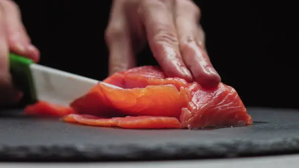 Sushi Chef Slices fresh Salmon on the sushi bar. Chef cutting salmon fillet at professional kitchen. Closeup chef hands slicing fresh fish slice in slow motion. Professional man cutting red fish.