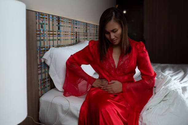 Have a pain under right waist. Have a pain under right waist. A woman in satin nightgown and red robes in pain holding his stomach and rib pain on right side in the bedroom at night. female rib cage stock pictures, royalty-free photos & images