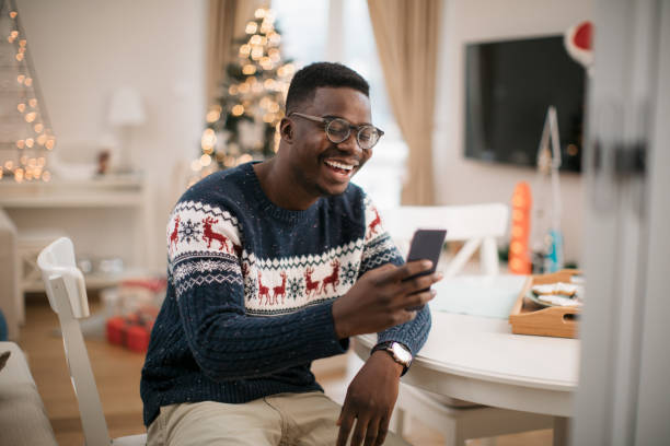 Staying in touch with friends and family during winter holidays Happy young African American man using a smart phone, staying in touch with his family and friends and wishing them a Marry Christmas and a happy new year christmas excitement stock pictures, royalty-free photos & images