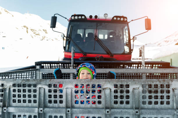 lindo adorable juguetón feliz niño dentro de rojo moderno snowcat ratrack snowplow box grooming de pie en la estación de esquí alpino pico ischgl austria. maquinaria pesada equipo de montaña vehículo de pista - box little boys bright car fotografías e imágenes de stock