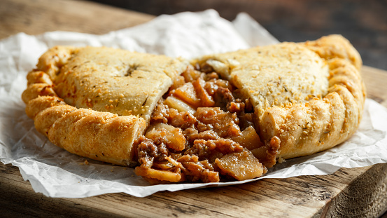 Traditional Cornish pasty filled with beef meat, potato and vegetables on black plate.