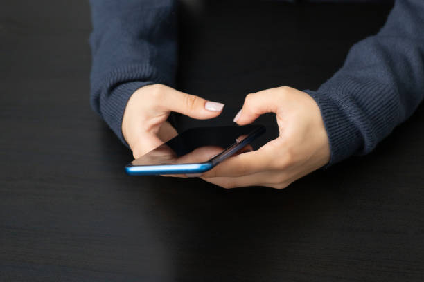 istock Women's hands with a mobile phone on a black table background 1280892344
