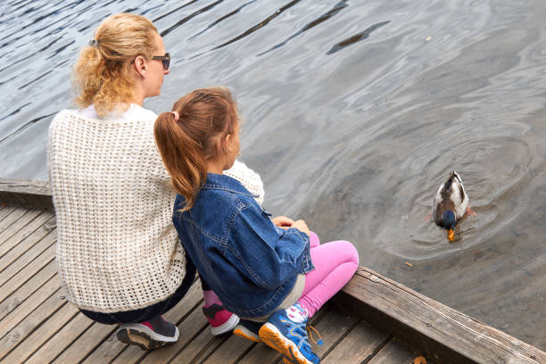 istock Mother and daughter feeding duck on a lake. 1280893324