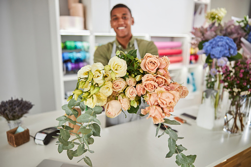 Waist up portrait of smiling handsome man holding bunch of blooming roses during working day in shop