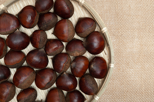 Chestnuts in bamboo basket isolated on jute background. Close-up. Copy space. Top view.