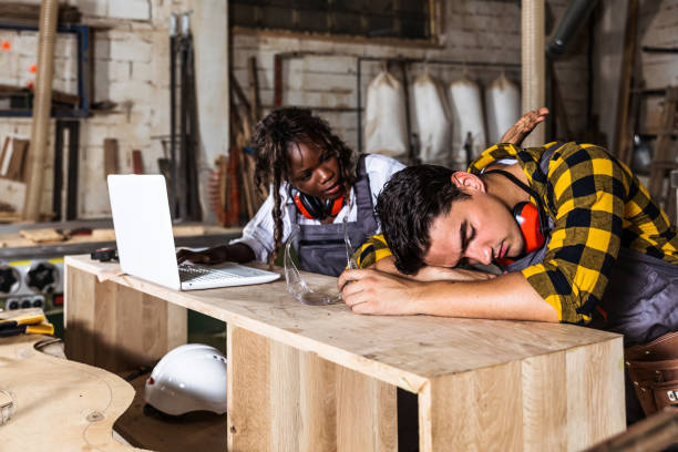 Man, you sleep while I work Two, male and female wood designer working with laptop in workshop trainee training computer designer stock pictures, royalty-free photos & images