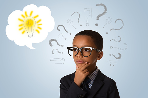 Adorable african little boy wearing glasses and thinking with many question marks and lightbulb. Concept of ideas